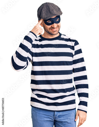 Young handsome man wearing burglar mask smiling pointing to head with one finger, great idea or thought, good memory © Krakenimages.com