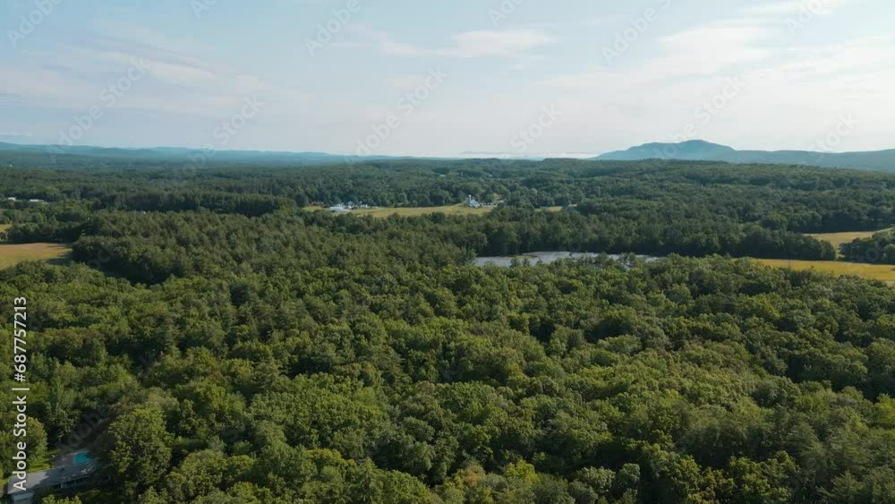 A calm drone shot of a thick green forest that has a little lake in the middle of it. Mountains can be seen in the far distance. A calm drone shot of a thick green forest that has a little lake in the middle of it. Mountains can be seen in the far distance.