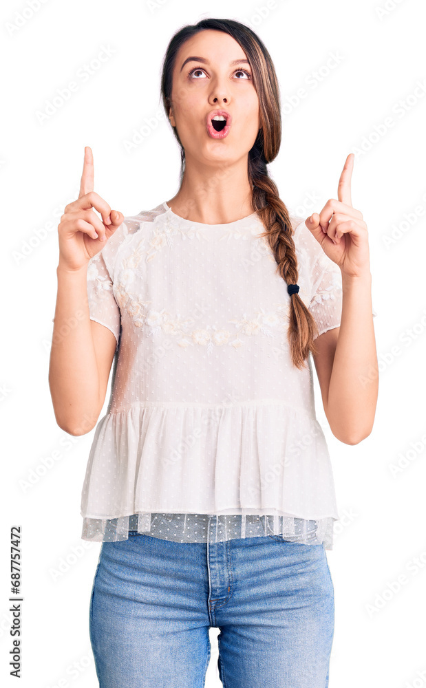 Young beautiful girl wearing casual t shirt amazed and surprised looking up and pointing with fingers and raised arms. Young beautiful girl wearing casual t shirt amazed and surprised looking up and pointing with fingers and raised arms.
