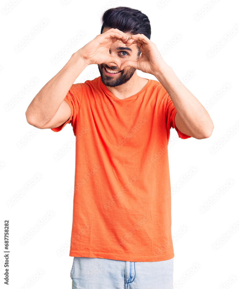 Young handsome man with beard wearing casual t-shirt doing heart shape with hand and fingers smiling looking through sign Young handsome man with beard wearing casual t-shirt doing heart shape with hand and fingers smiling looking through sign