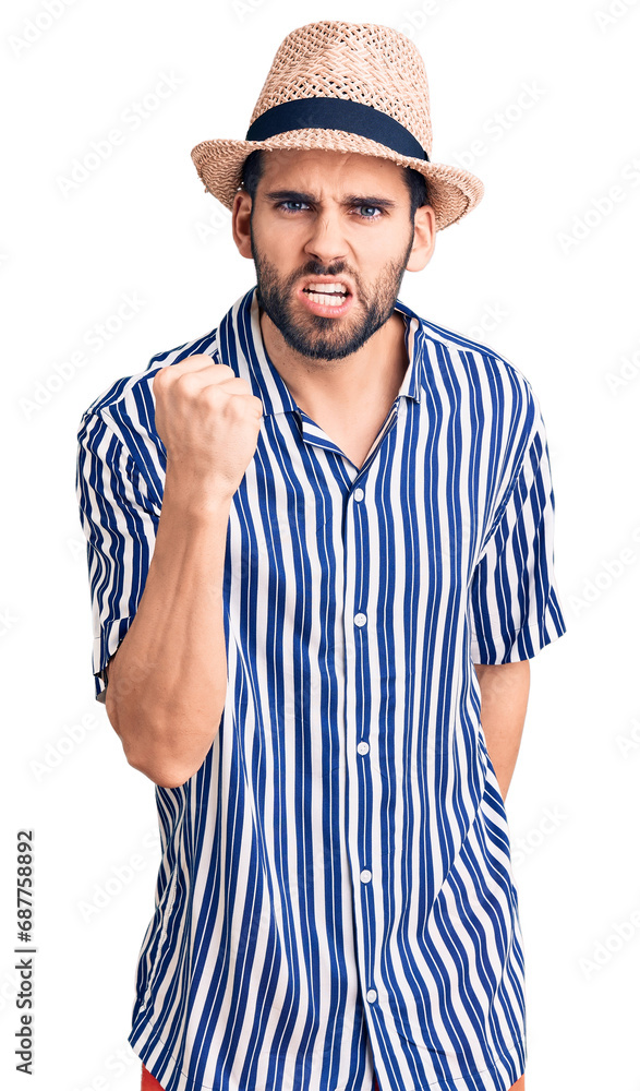Young handsome man with beard wearing summer hat and striped shirt angry and mad raising fist frustrated and furious while shouting with anger. rage and aggressive concept. Young handsome man with beard wearing summer hat and striped shirt angry and mad raising fist frustrated and furious while shouting with anger. rage and aggressive concept.