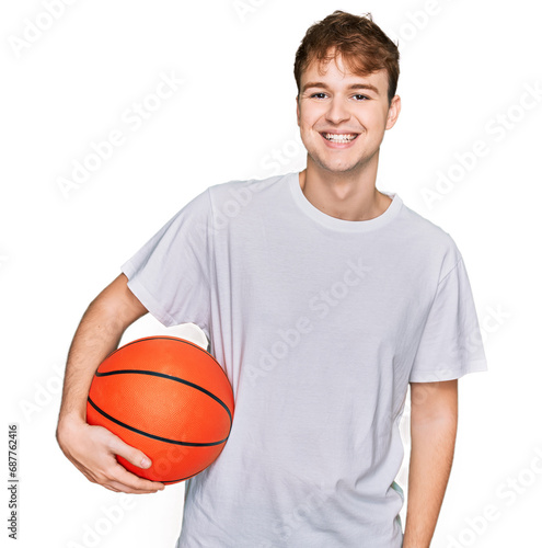 Young caucasian man holding basketball ball looking positive and happy standing and smiling with a confident smile showing teeth