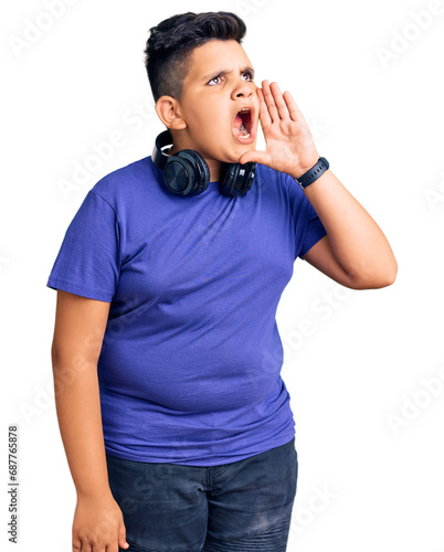 Little boy kid listening to music wearing headphones shouting and screaming loud to side with hand on mouth. communication concept.