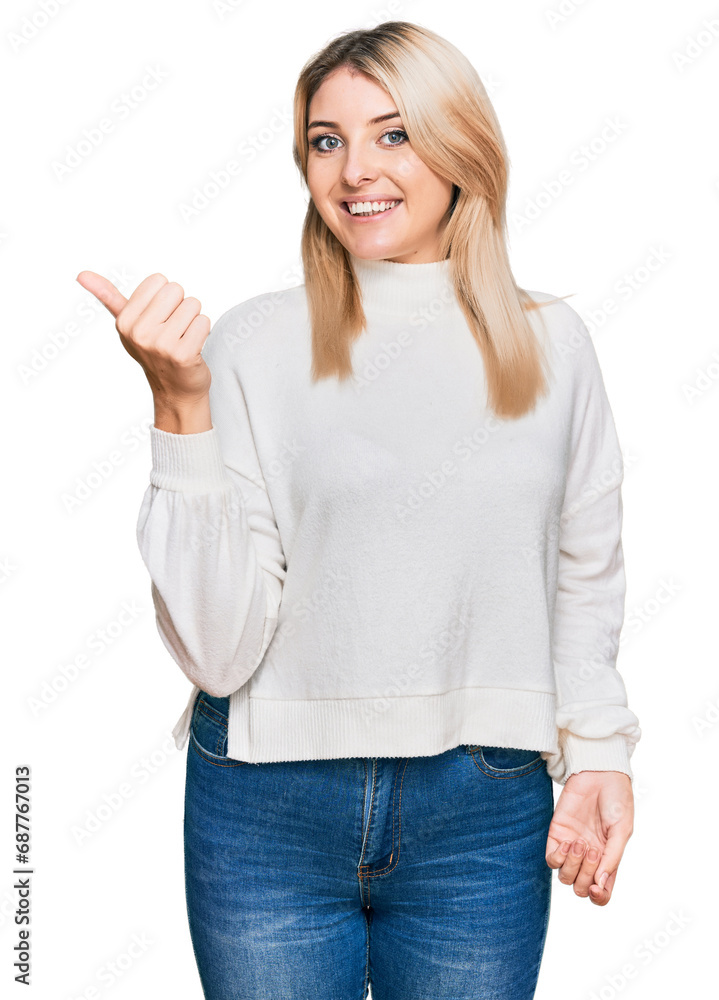 Young caucasian woman wearing casual winter sweater smiling with happy face looking and pointing to the side with thumb up. Young caucasian woman wearing casual winter sweater smiling with happy face looking and pointing to the side with thumb up.