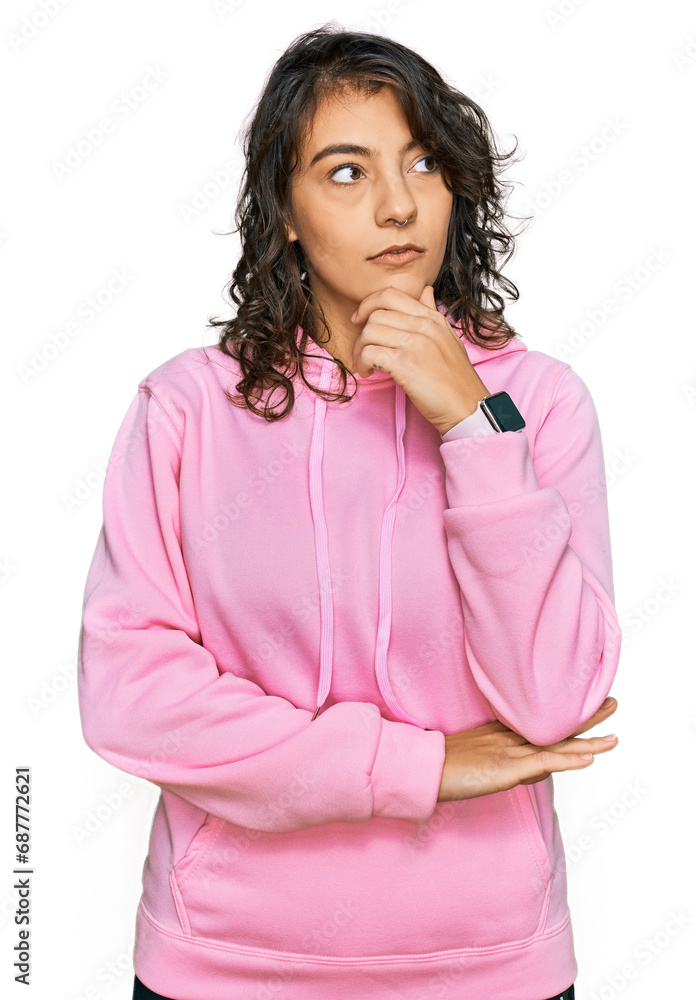 Young hispanic woman wearing casual sweatshirt with hand on chin thinking about question, pensive expression. smiling with thoughtful face. doubt concept. Young hispanic woman wearing casual sweatshirt with hand on chin thinking about question, pensive expression. smiling with thoughtful face. doubt concept.