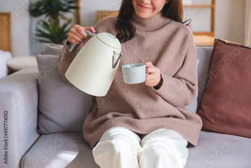 Closeup image of a young woman pouring hot water from electric kettle in to a cup at home photo