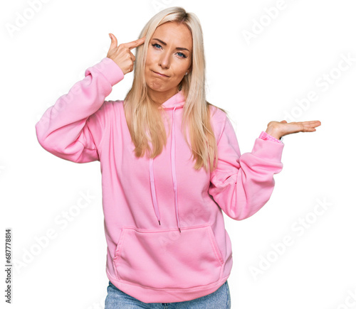 Young blonde woman wearing casual sweatshirt confused and annoyed with open palm showing copy space and pointing finger to forehead. think about it.