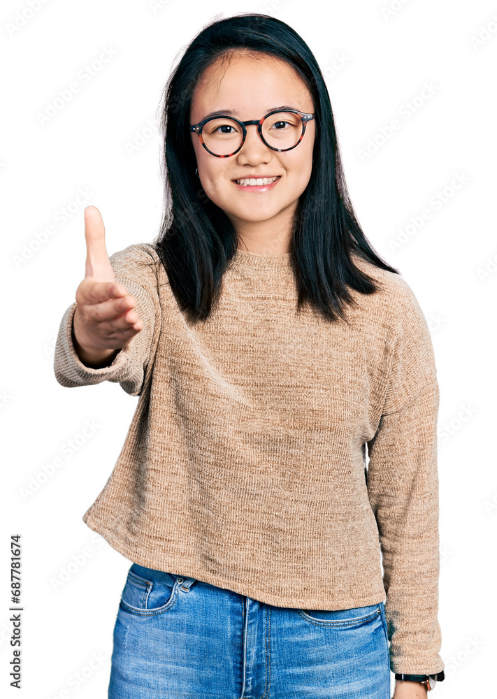 Young chinese woman wearing casual sweater and glasses smiling friendly offering handshake as greeting and welcoming. successful business.