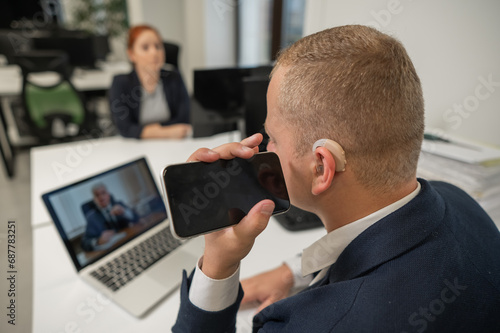 Caucasian man with a hearing aid talking on the phone on speakerphone. 