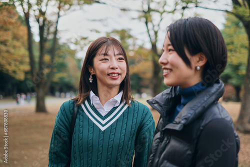 秋の公園で笑顔で話をする仲の良い女性二人
