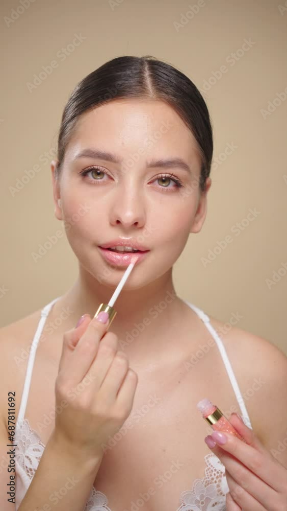 Beauty brunette woman applying lip gloss isolated on beige background. Vertical video. Makeup cosmetics Beauty brunette woman applying lip gloss isolated on beige background. Vertical video. Makeup cosmetics