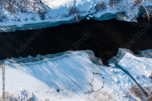 View from above on the bed of a freezing river among snow-covered winter nature