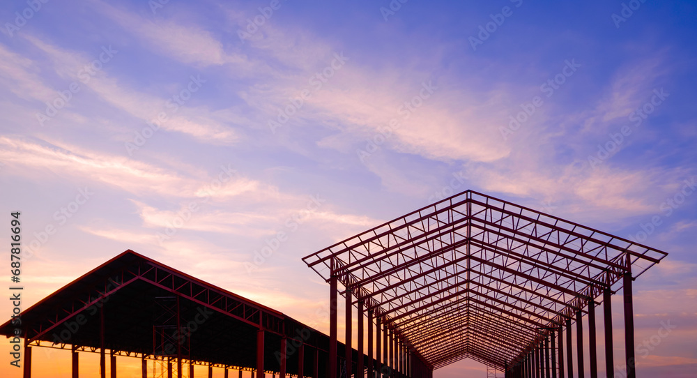 Silhouette two metal industrial building outlines in construction site area against sunset sky background, front view with copy space