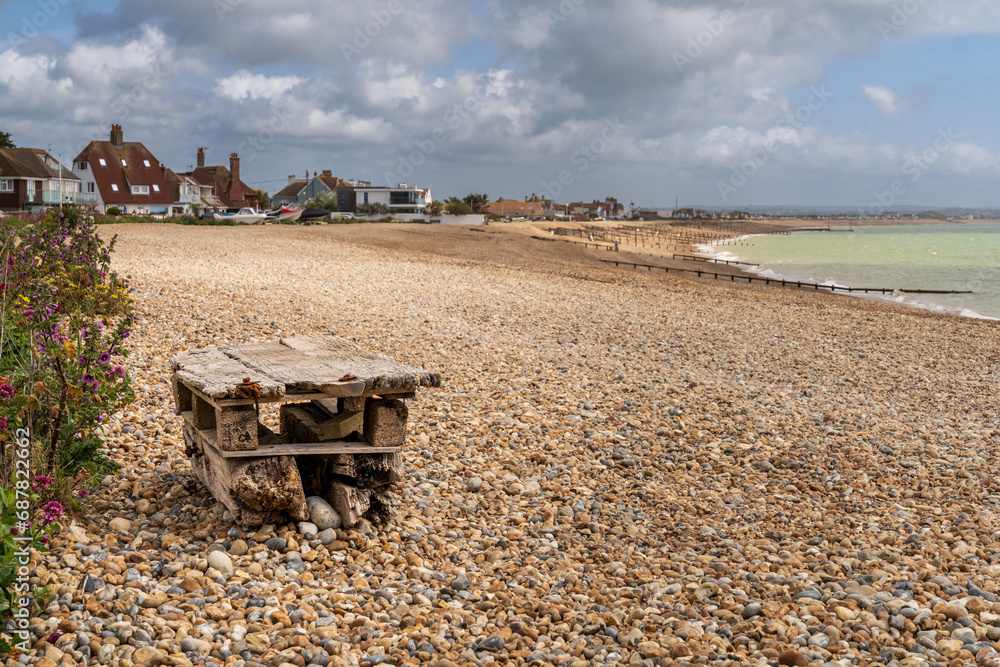 Obraz premium The pebble beach in Pevensey Bay, East Sussex, England, with two pallets nailed one on top of the other to be used as a bench