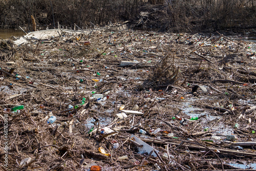 A large garbage jam blocking the riverbed with a pile of dry branches and an accumulation of plastic waste. Pollution of the environment with non-degradable waste