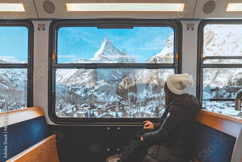 Happy Tourist woman looking out the window enjoying with the snow Matterhorn mountain while sitting in the train, Zermatt in Switzerland. photo