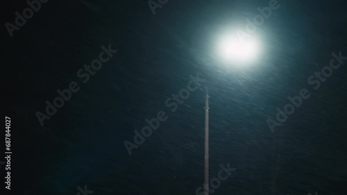Slow motion footage of snowflakes dancing in wind and falling on ground in winter. Snow storm against alone bight street lamp at night. Fabulous blizzard on Christmas Eve. Stormy winter background.  photo