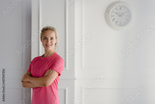 Portrait of a beautiful smiling athletic woman ready for daily sports training in a room with white walls and a clock