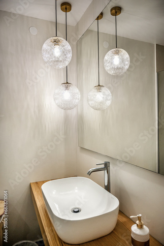 Modern Bathroom. Stylish sink is perched atop wooden shelves. The focal point is accentuated by the subtle elegance of glass ball ceiling lamps.