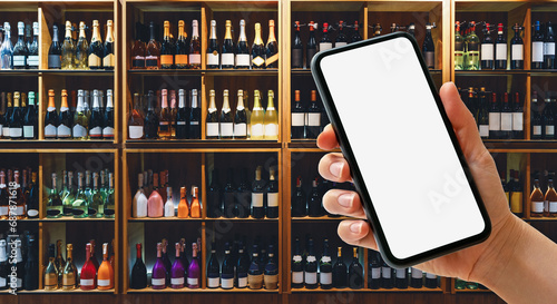 Принти на полотні Smart phone with blank screen in female hand in front of shelves with wine bottles in liquor store
