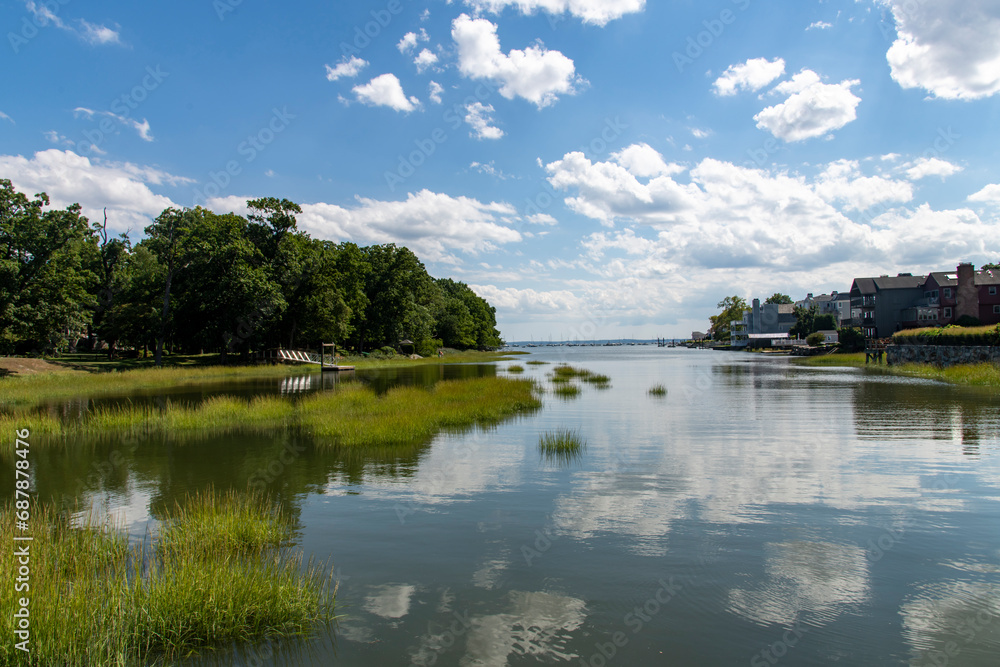 View over the tranquil water of Smith Cove in Greenwich, CT, USA with view towards the Long Island sound and large cumulus clouds in blue sky reflected in water