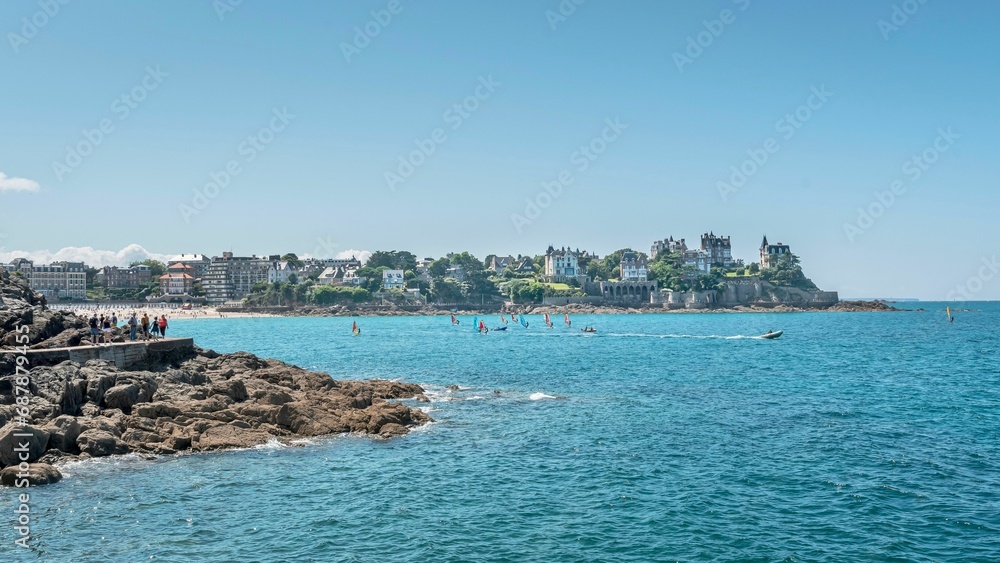 Crowd of people are gathered on a rocky beach overlooking the ocean in Saint-Malo, France