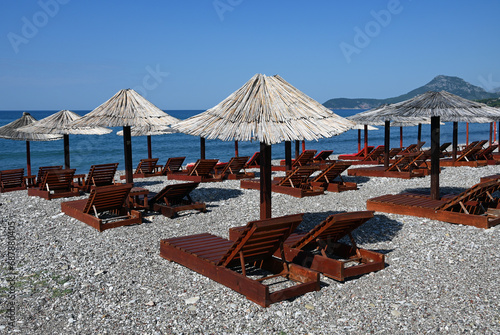 Bar, Montenegro, Dalmatia, Balkans, Europe - 09.2023 : shingle beach, sun loungers, parasols,  blue sky, Adriatic Sea and Dinaric Alps in background photo