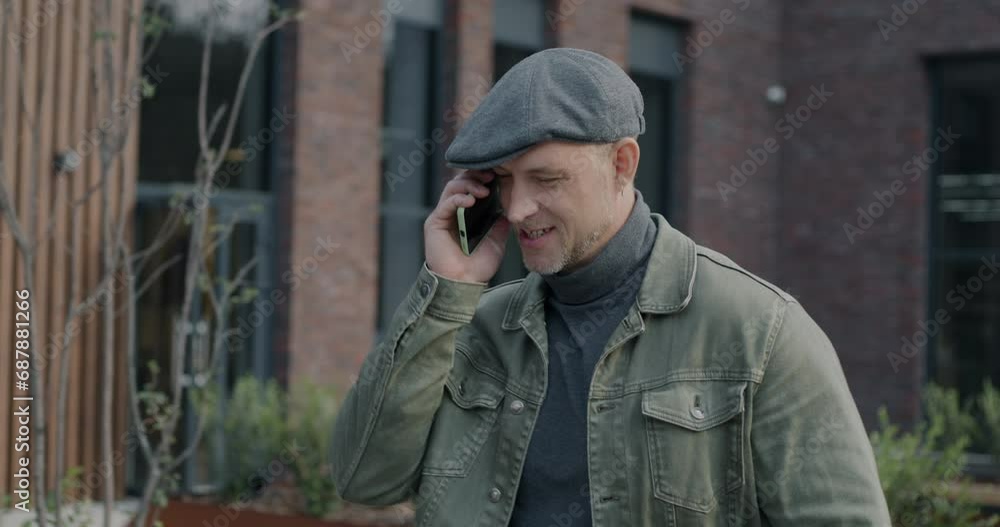 Joyful young man walking in city and talking on mobile phone discussing funny news laughing. Cellphone communication and urban people concept. Joyful young man walking in city and talking on mobile phone discussing funny news laughing. Cellphone communication and urban people concept.