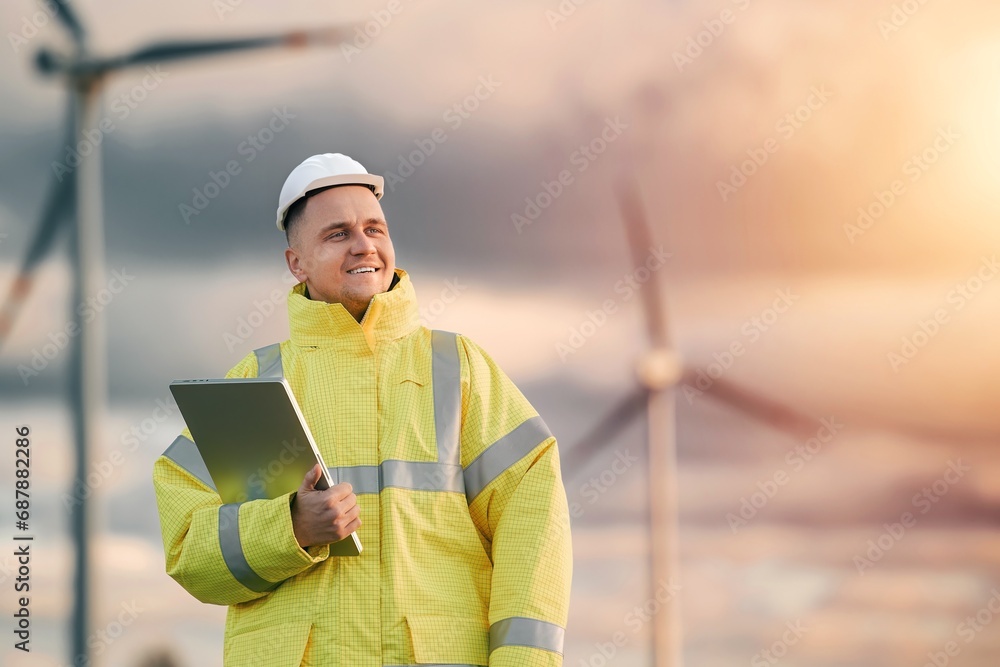 A technician in a yellow jacket uses a tablet to monitor and install wind turbines and solar panels on a farm. Sustainable energy engineering project that aims to produce clean renewable electricity