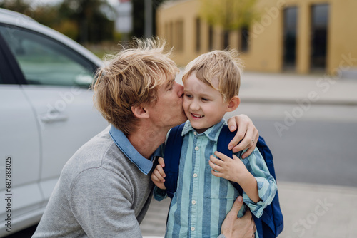 Father saying goodbyeto to son in front of school building, hugging him and kissing him on the cheek. Dad heading to work. Concept of work-life balance for parents.