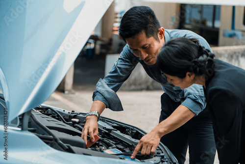 Man help woman fix the car problem. He pop up the car hood to repair the damaged part. uds