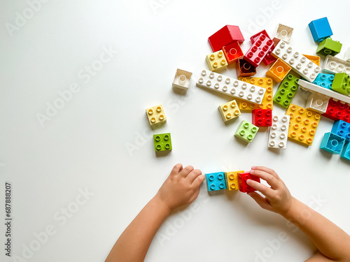 Child playing with colorful building blocks on white background. Top view