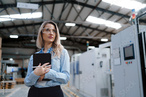 Female manager standing in modern industrial factory. Manufacturing facility with robotics and automation. Female leader, CEO in heavy industry, manufactury. photo