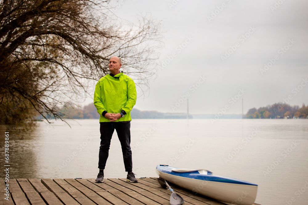 Mid aged sporty man wearing dry suit and standing on the jetty by the river