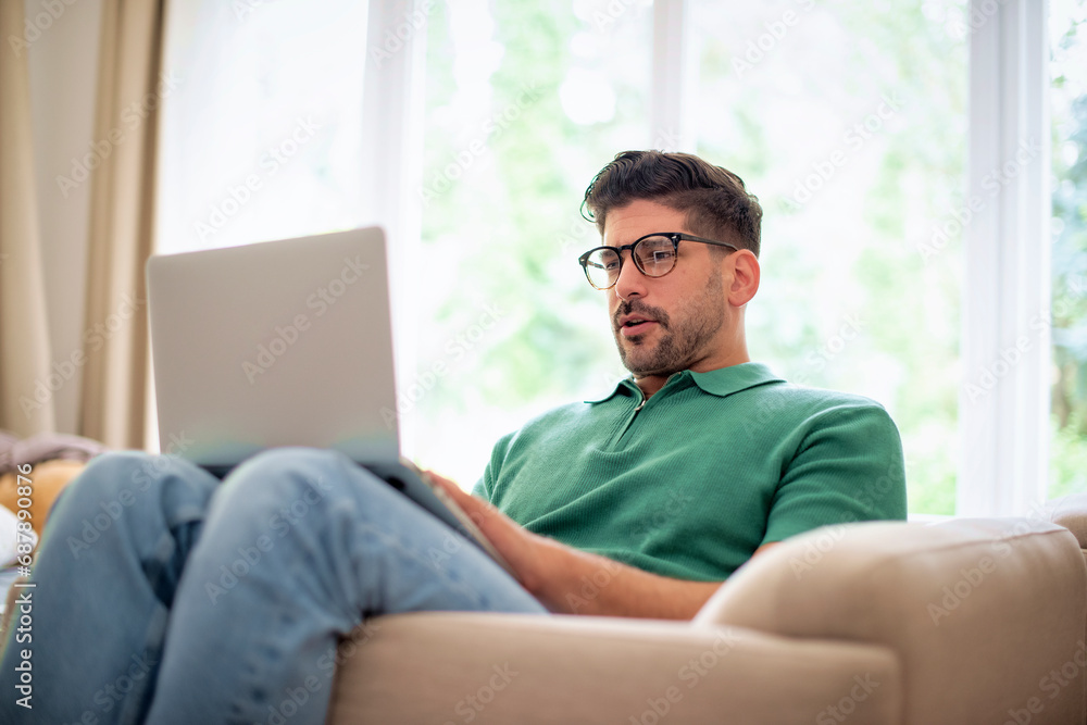 Confident mid aged man sitting in an armchair at home and using laptop for work Confident mid aged man sitting in an armchair at home and using laptop for work