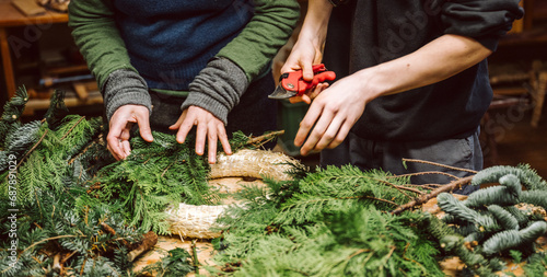 Hände von zwei Menschen halten Draht, Zange und Adventskranz. Mensch bastelt einen weihnachtlichen Adventskranz.