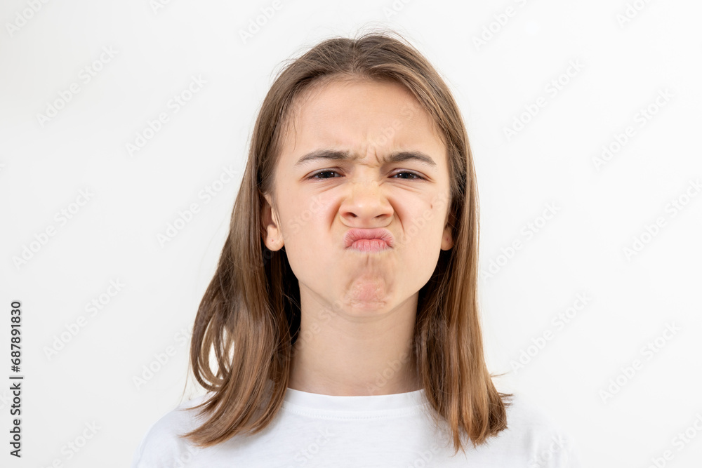 A teenager girl grimaces with displeasure on a white background, isolated. A teenager girl grimaces with displeasure on a white background, isolated.