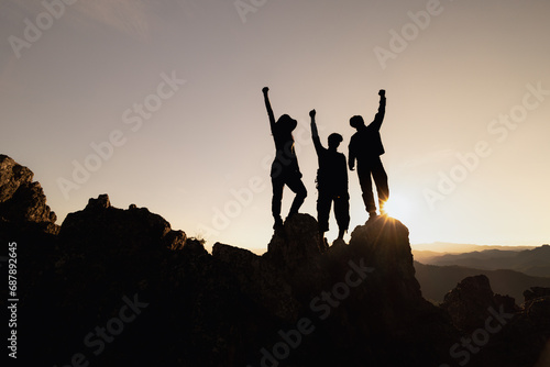 Happy friends hikers or tourists stands with raised arms on mountain top against mountains and looking at sunset. Independent hiking travel, success.