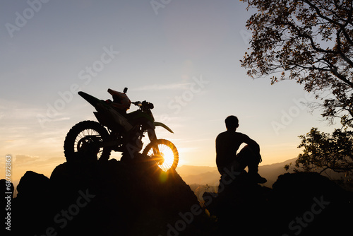 Man with motocross bike against beautiful lights, silhouette of a man with motocross motorcycle On top of rock high mountain at beautiful sunset, enduro motorcycle travel concept.