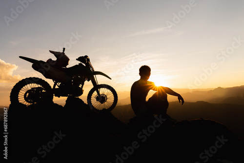 Man with motocross bike against beautiful lights, silhouette of a man with motocross motorcycle On top of rock high mountain at beautiful sunset, enduro motorcycle travel concept. © Tinnakorn