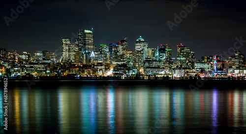 A vibrant city skyline at night with illuminated buildings and reflections.