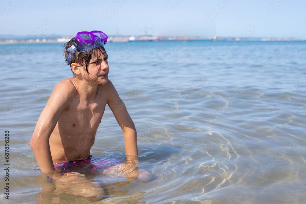 Handsome teenager with a diving mask, capturing the carefree spirit of a summer day at the beach sitting in the sea water,copyspace..