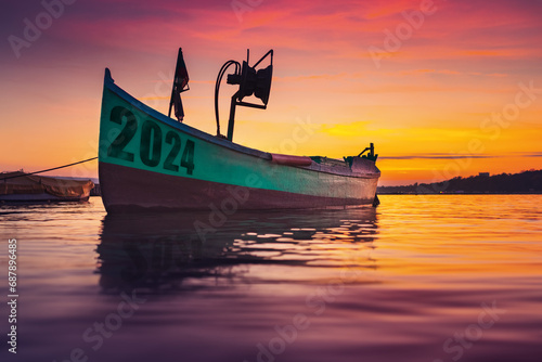 2024 Fishing boat on beach shore and sunset reflection in water 