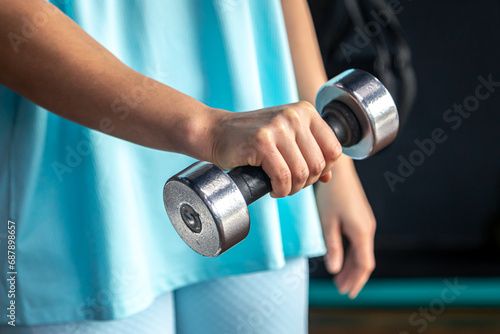 Small dumbbell in the hands of a woman in the gym, close up.