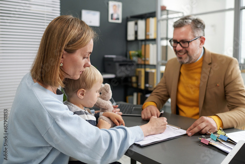 Tableau sur toile Young woman sitting with her little son and filing documents for social benefits