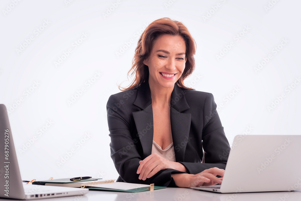 Studio shot of an attractive mid aged businesswoman sitting at desk and using laptops against isolated background Studio shot of an attractive mid aged businesswoman sitting at desk and using laptops against isolated background