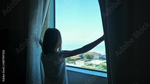Girl openning window curtains and looking to the horizon. The beginning of the day concept. 4k video footage photo