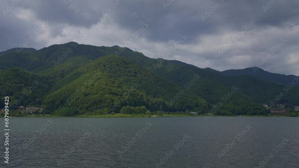 Traverse the serene lake, where the vista unfolds with green hills cascading into the Japanese waters from the boat's viewpoint during a cloudy day Traverse the serene lake, where the vista unfolds with green hills cascading into the Japanese waters from the boat's viewpoint during a cloudy day