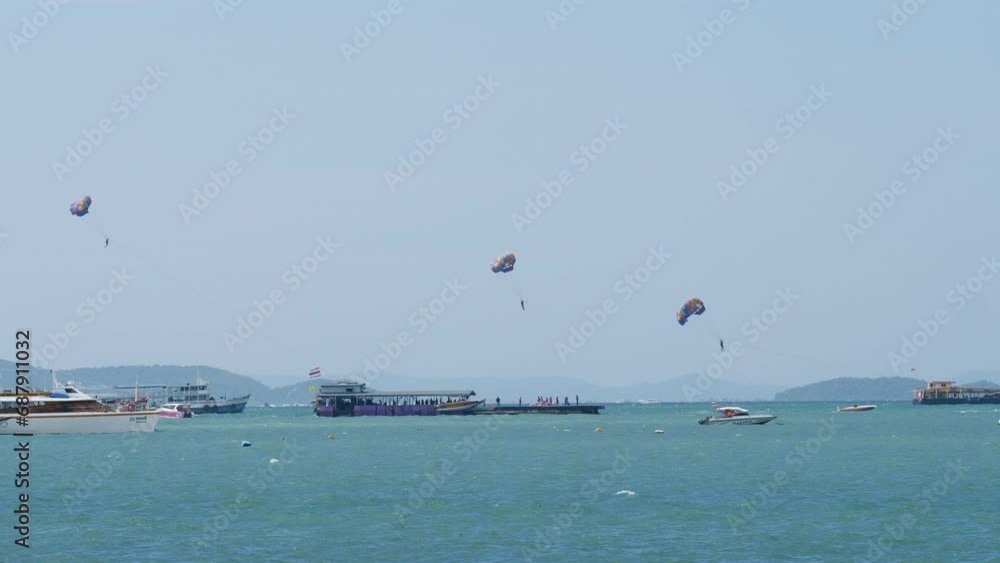 Three people parasailing in Pattaya as they are being pulled by boat to gain altitude while are other boats are seen, Thailand Three people parasailing in Pattaya as they are being pulled by boat to gain altitude while are other boats are seen, Thailand