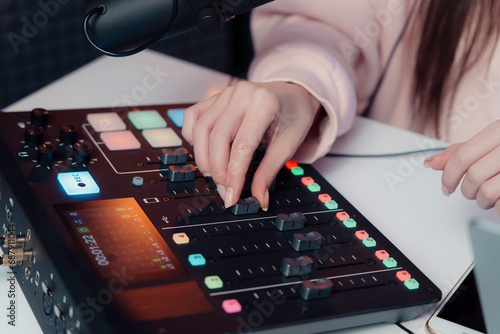 Close-up of a podcaster's hands as she expertly adjusts an audio mixer, fine-tuning the sound for a live podcast recording